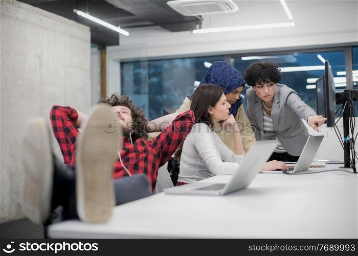 young software developer resting with legs on desk while his multiethnics business team writing programming code in the background at startup office