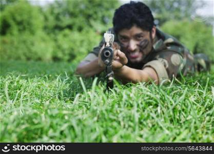 Young soldier aiming with rifle while lying on grass