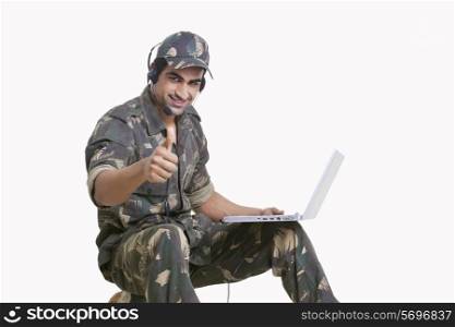 Young soldier using laptop and showing thumbs up sign
