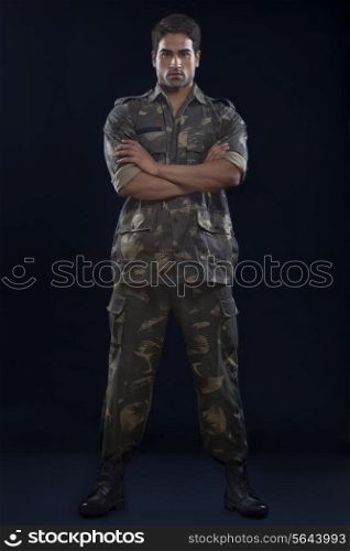 Young soldier with arms crossed standing over blue background