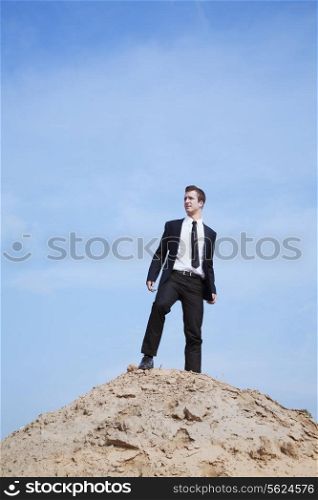 Young solitary businessman standing on a hill in the desert