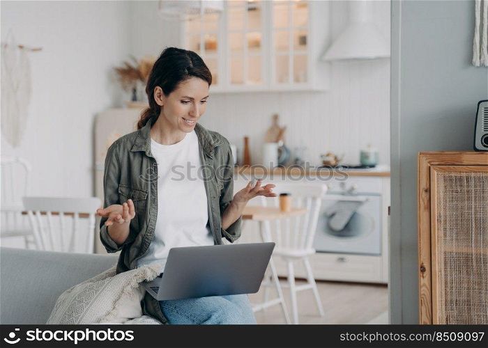 Young spanish woman has conversation on computer. Businesswoman has corporate internet group call. Girl staying home and sitting on sofa in living room. Online meeting on quarantine.. Young spanish woman has conversation on computer. Businesswoman has corporate group call at home.