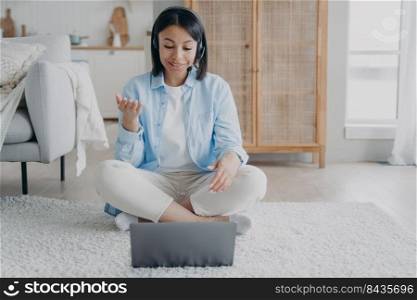 Young spanish woman in headset with microphone has video conference on laptop. Girl is speaking and streaming video. Distant learning from home. Virtual yoga or fitness lesson, internet session.. Young spanish woman in headset with microphone has video conference and streaming video.