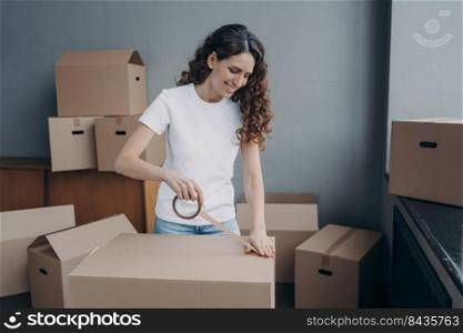 Young spanish woman is packing boxes with duct tape. Moving service business. Lady is wrapping cardboard boxes with packing tape. Female worker preparing boxes for shipping and storage.. Young spanish woman is packing boxes with duct tape. Moving service business.