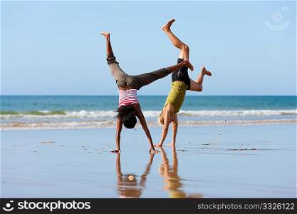 Young sport couple - Caucasian man and African-American woman - doing gymnastics on the beach