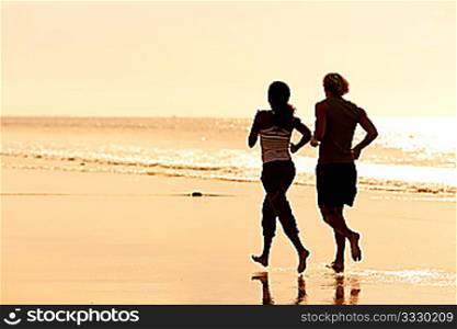 Young sport couple - jogging on the beach in sunset