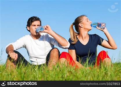 Young sport couple was jogging on a green summer meadow but is resting now, replenishing themselves with a zip of water