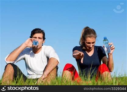 Young sport couple was jogging on a green summer meadow but is resting now, replenishing themselves with a zip of water
