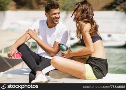 Young sporting couple hydrate themselves with water in metal bottles while taking a break after sport.. Two fitness people hydrate themselves with water in metal cans while taking a break after sport.