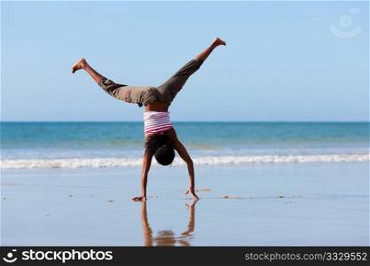 Young sportive African-American woman doing gymnastics on the beach