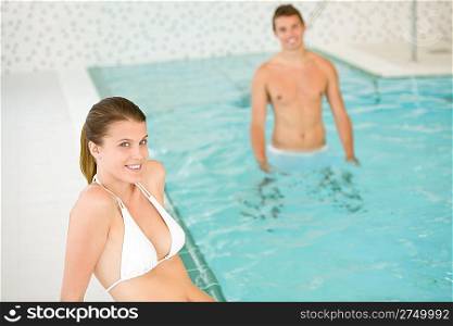 Young sportive couple relax in swimming pool, focus on woman in bikini