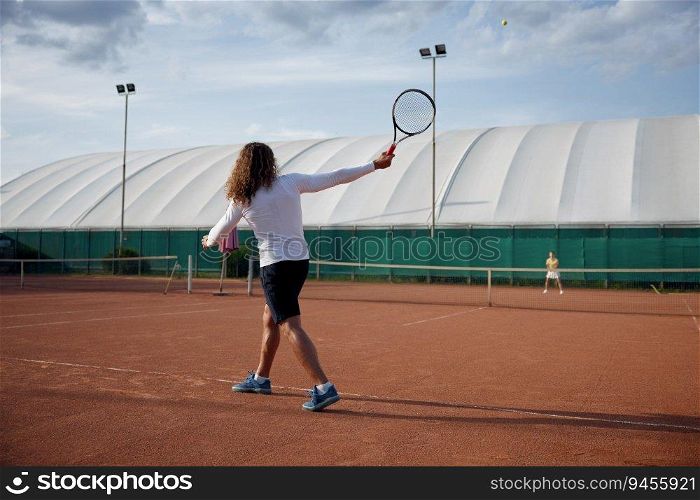Young sports woman and man playing tennis match on outdoor court during sunny day. Training class concept. Young sports woman and man playing tennis on outdoor court