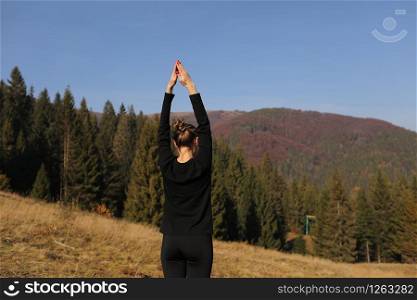 Young sports woman doing yoga exercise on the mountains and sky background in the autumn.. Young sports woman doing yoga exercise on the mountains and sky background in the autumn