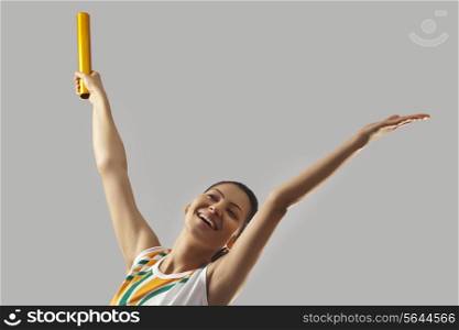 Young sports woman with relay baton celebrating victory isolated over gray background