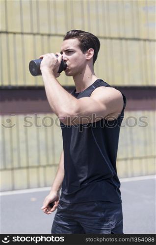 Young sportsman drinking water after jogging