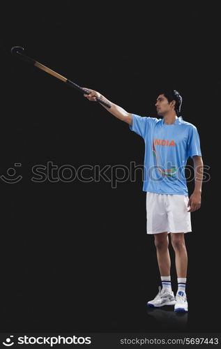 Young sportsman raising hockey stick isolated over black background