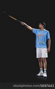 Young sportsman raising hockey stick isolated over black background