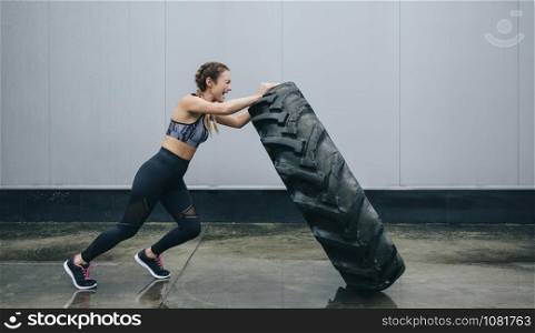 Young sportswoman doing cross-training lifting a tire on a rainy day. Sportswoman doing cross-training lifting a tire