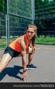 Young sportswoman doing leg stretches on a sports court. Sportswoman doing leg stretches