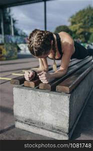 Young sportswoman doing plank on a bench outdoors on a rainy day. Sportswoman doing plank on a bench