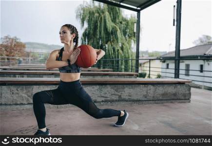 Young sportswoman doing stride exercises with a basketball outdoors. Sportswoman doing stride exercises with basketball