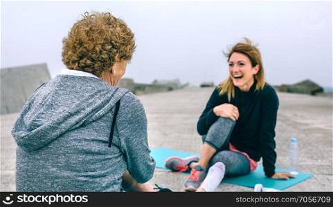 Young sportswoman laughing with senior woman by sea pier. Sportswoman laughing with senior woman