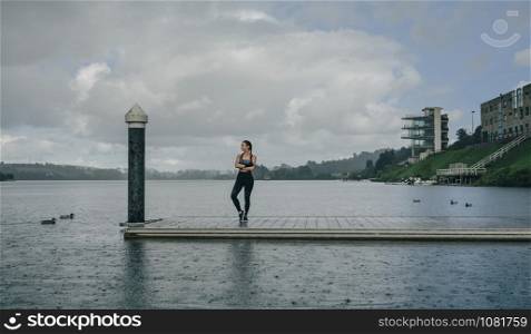 Young sportswoman looking at the lake from the pier under the rain. Sportswoman looking lake from pier
