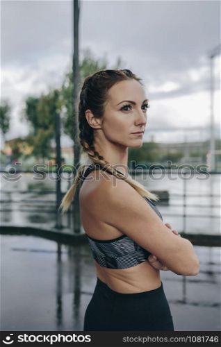 Young sportswoman posing arms crossed outdoors on a rainy day. Sportswoman posing arms crossed