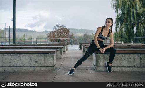 Young sportswoman posing sitting on a bench outdoors. Sportswoman posing sitting on a bench
