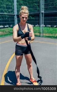 Young sportswoman putting on boxing bandages to train outdoors. Sportswoman putting on boxing bandages