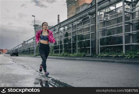 Young sportswoman running on a rainy day in an industrial zone. Sportswoman running in an industrial zone