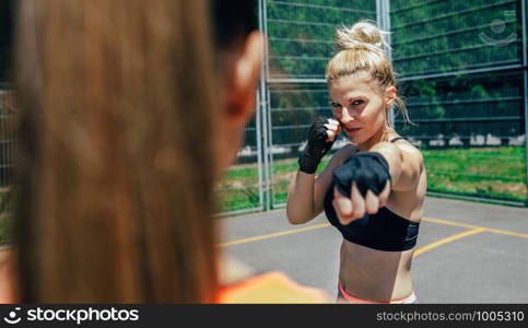 Young sportswoman training boxing with her trainer outside. Sportswoman training boxing with her trainer