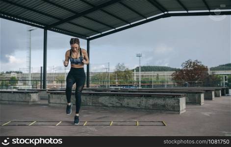 Young sportswoman training jumping on an agility ladder outdoors. Sportswoman jumping on an agility ladder
