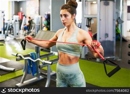 Young sportswoman warming up with fitness gums in the gym wearing sportswear. Young sportswoman warming up with fitness gums in the gym