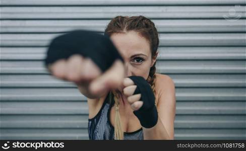 Young sportswoman with boxing bandages looking at camera and punching. Focus on face in background. Sportswoman looking at camera and punching