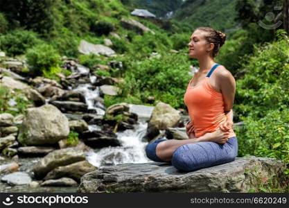 Young sporty fit woman doing yoga - meditating in Baddha Padmasana  Bound Lotus Pose  outdoors at tropical waterfall. Young fit woman doing yoga oudoors at waterfall