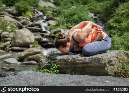 Young sporty fit woman doing yoga - meditating in Baddha Padmasana  Bound Lotus Pose  outdoors at tropical waterfall. Young woman does yoga oudoors at waterfall