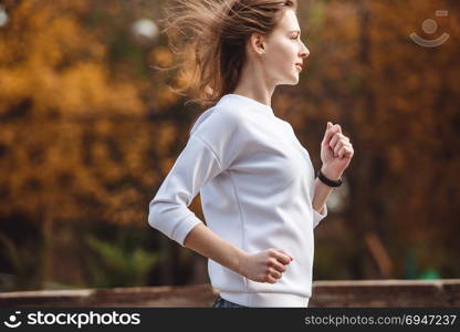 Young sporty girl jogging in city park at autumn day.. Young sporty girl jogging in city park at autumn day