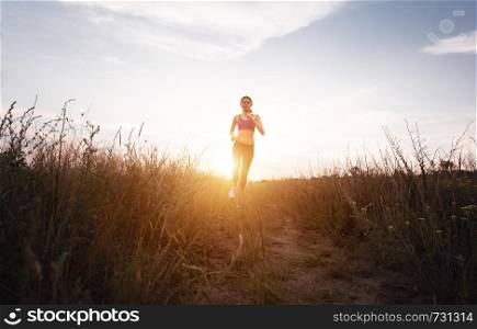 Young sporty girl running on a rural road at sunset in summer field. Lifestyle sports background