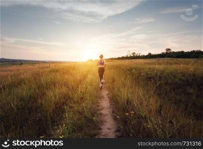 Young sporty girl running on a rural road at sunset in summer field. Lifestyle sports background
