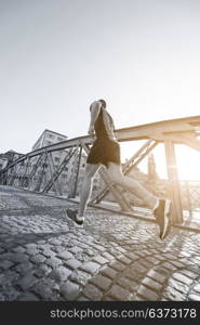 young sporty man jogging across the bridge at sunny morning in the city