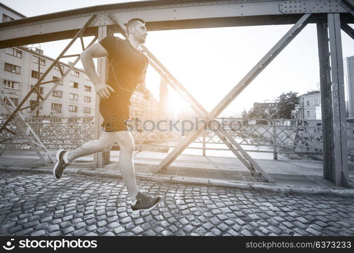 young sporty man jogging across the bridge at sunny morning in the city