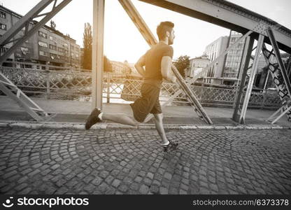 young sporty man jogging across the bridge at sunny morning in the city