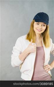 Young sporty teenage looking woman wearing cap and sportswear enjoying workout results. Studio shot on grey background. Happy woman wearing sporty outfit