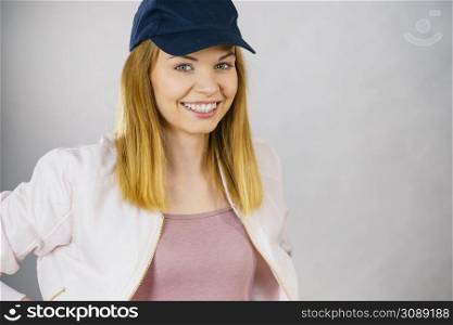 Young sporty teenage looking woman wearing cap and sportswear enjoying workout results. Studio shot on grey background. Happy woman wearing sporty outfit
