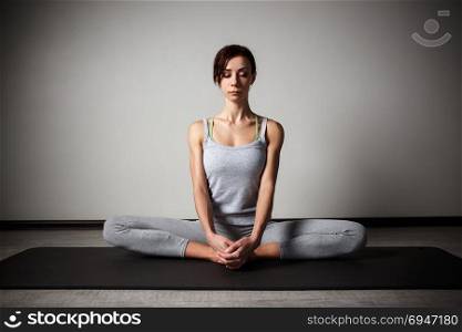 Young sporty woman doing yoga stretching exercise sitting in gym near bright windows. Young sporty woman doing yoga stretching exercise sitting in gym near bright windows.