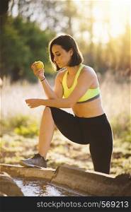 Young sporty woman eating an apple in the field at sunset after running