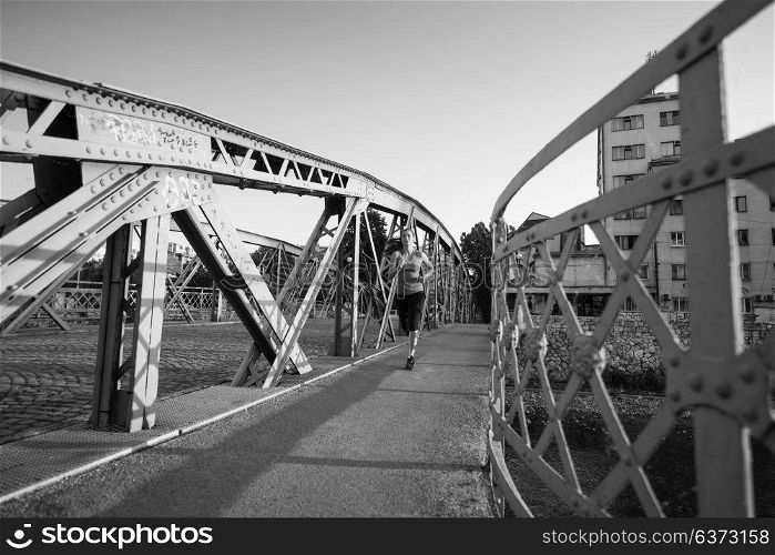 young sporty woman jogging across the bridge at sunny morning in the city