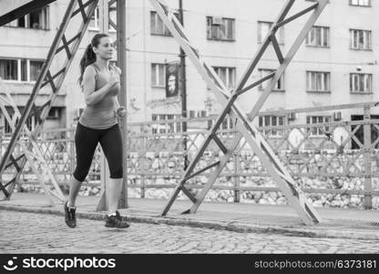 young sporty woman jogging across the bridge at sunny morning in the city