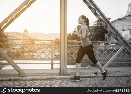 young sporty woman jogging across the bridge at sunny morning in the city